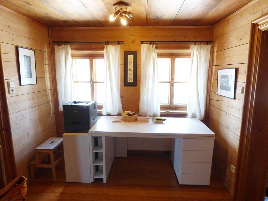 Helles Arbeitszimmer mit Holzwänden, Holzboden und zwei Fenstern.