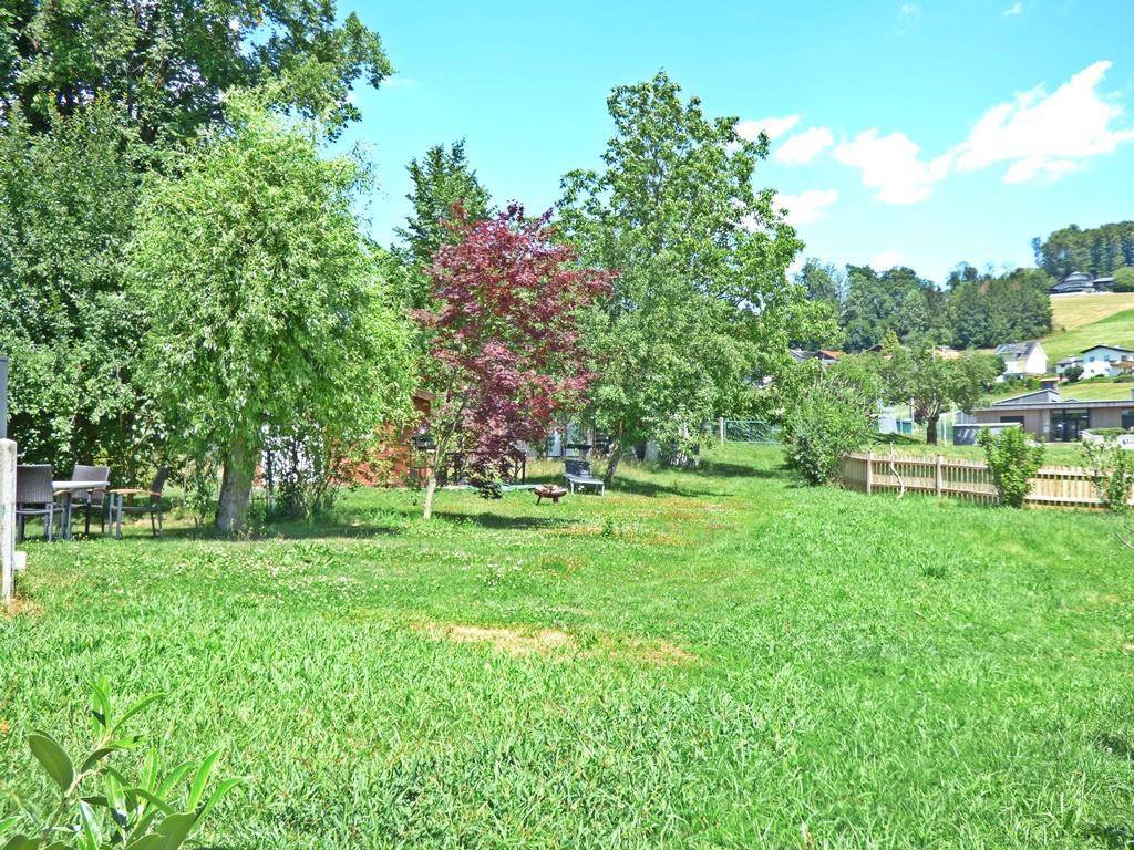 Weitläufiger Garten mit Rasen, verschiedenen Bäumen und Blick auf die Umgebung.