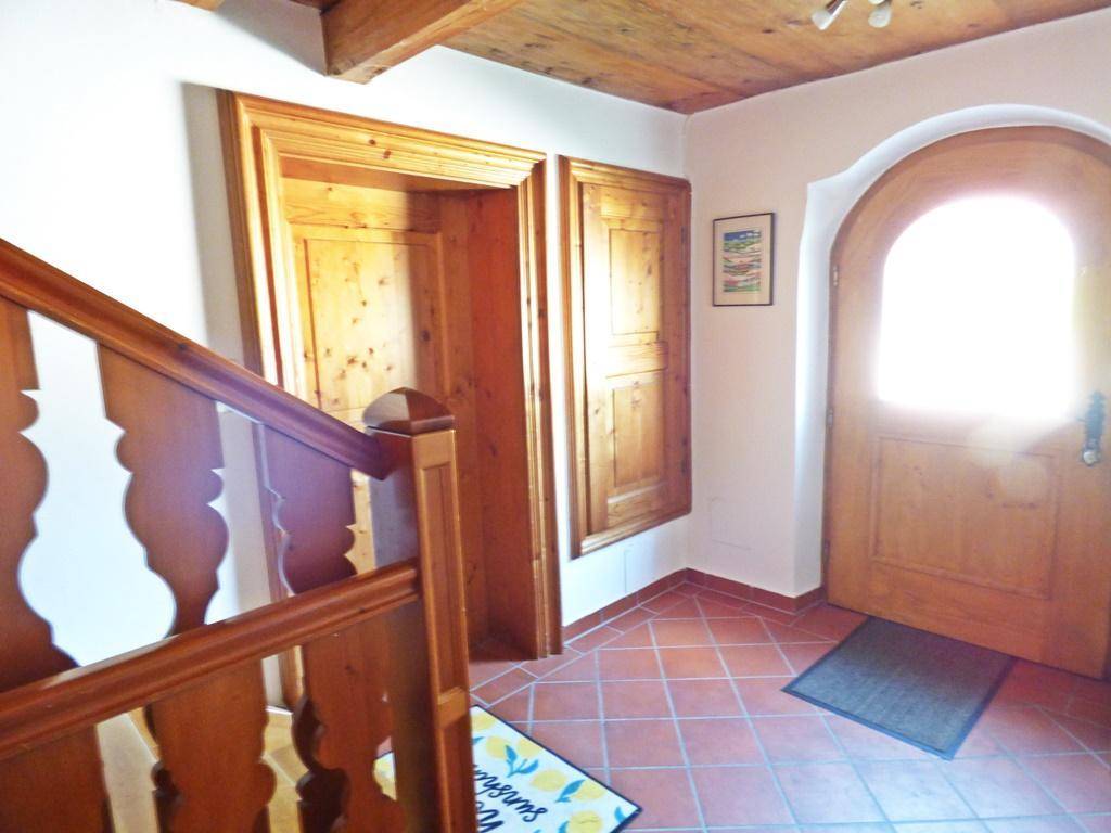 Heller Eingangsbereich mit Holztür, Holztreppe und Terrakottafliesen.