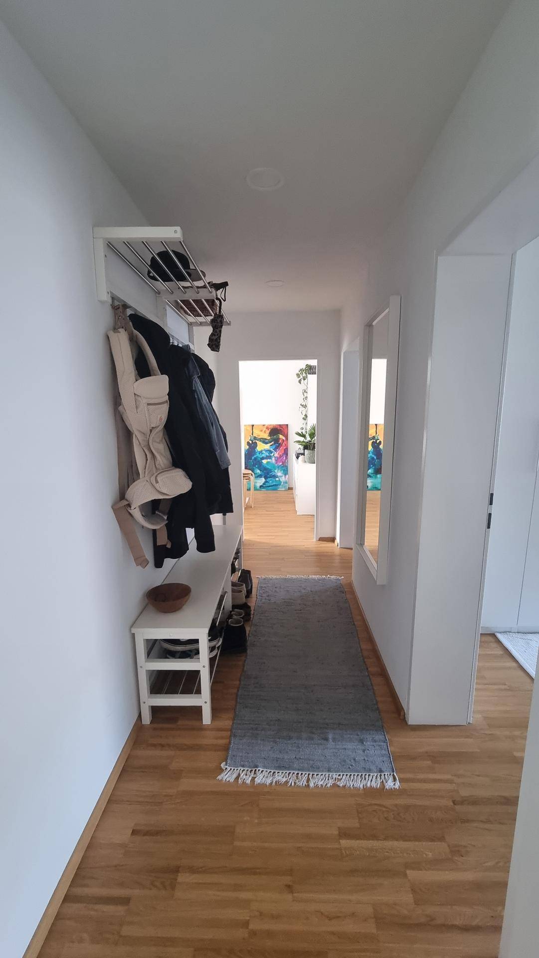 Heller Flur mit Garderobe, Schuhbank und Spiegeln, der zu weiteren Räumen führt.
