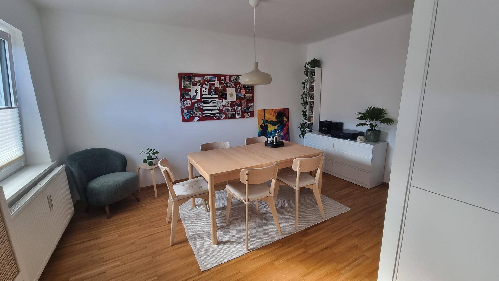 Essbereich mit hellem Holztisch, Stühlen und einem gemütlichen Sessel am Fenster.