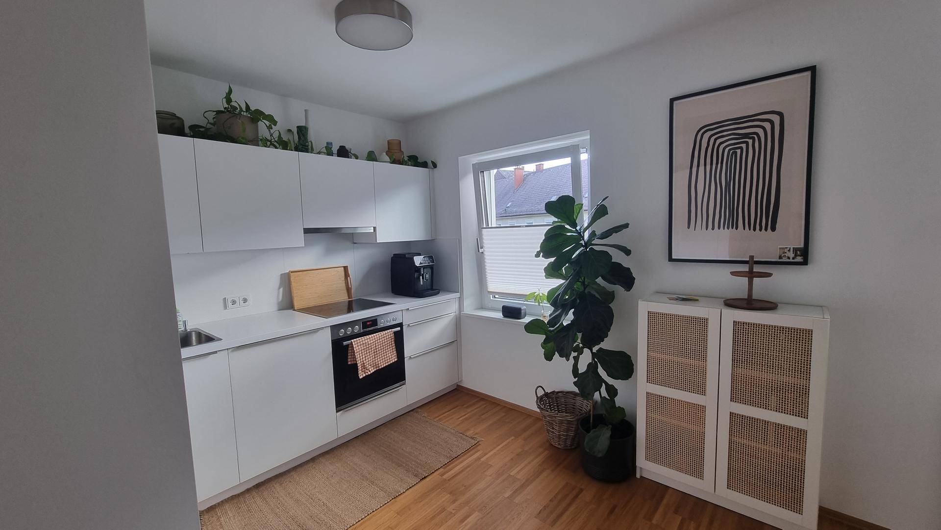 Helle Küche mit weißen Einbauschränken, modernen Geräten und einem dekorativen Schrank.