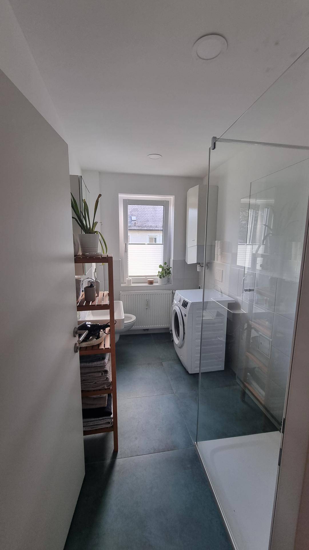 Modernes Badezimmer mit ebenerdiger Dusche, Toilette, Waschmaschine und Fenster.