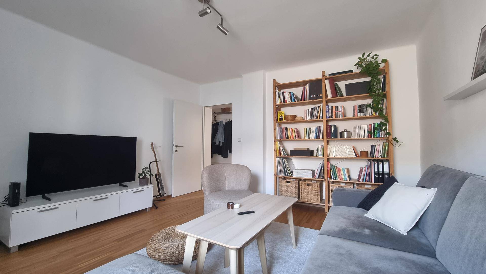 Helles Wohnzimmer mit großem Fernseher, Sofa und einem Bücherregal aus Holz.