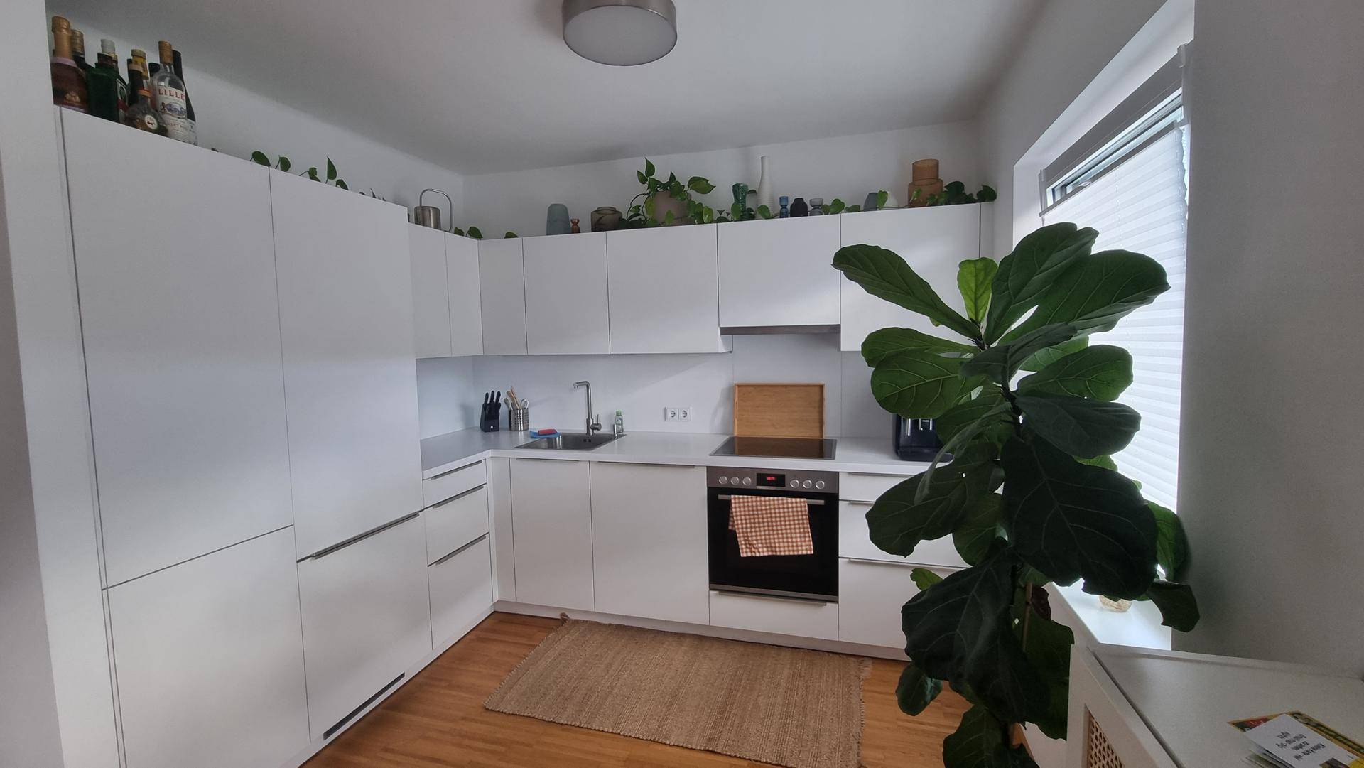 Moderne Küche mit weißen Schränken, integrierten Geräten und einem Fenster.