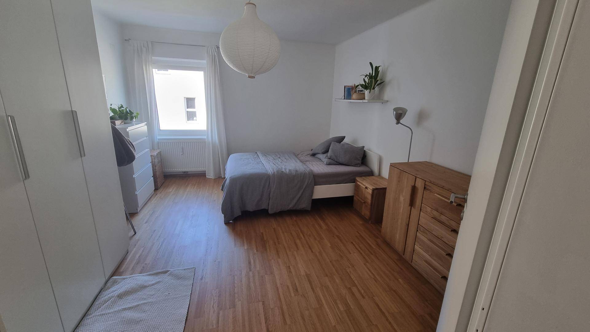 Helles Schlafzimmer mit Bett, großem Kleiderschrank und einem Fenster für viel Tageslicht.