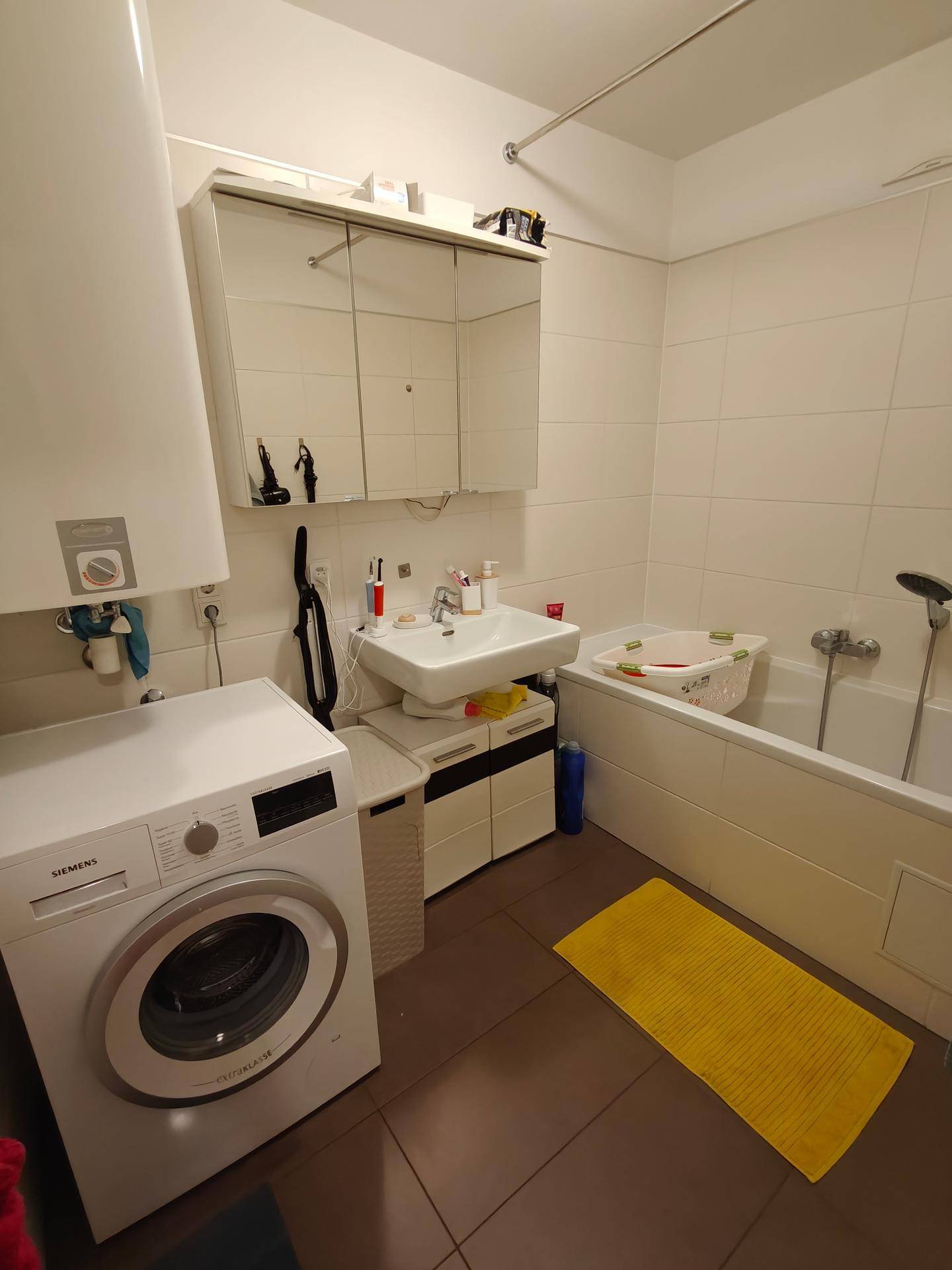 Funktionales Badezimmer mit Badewanne, Waschbecken, Spiegelschrank und Waschmaschine.