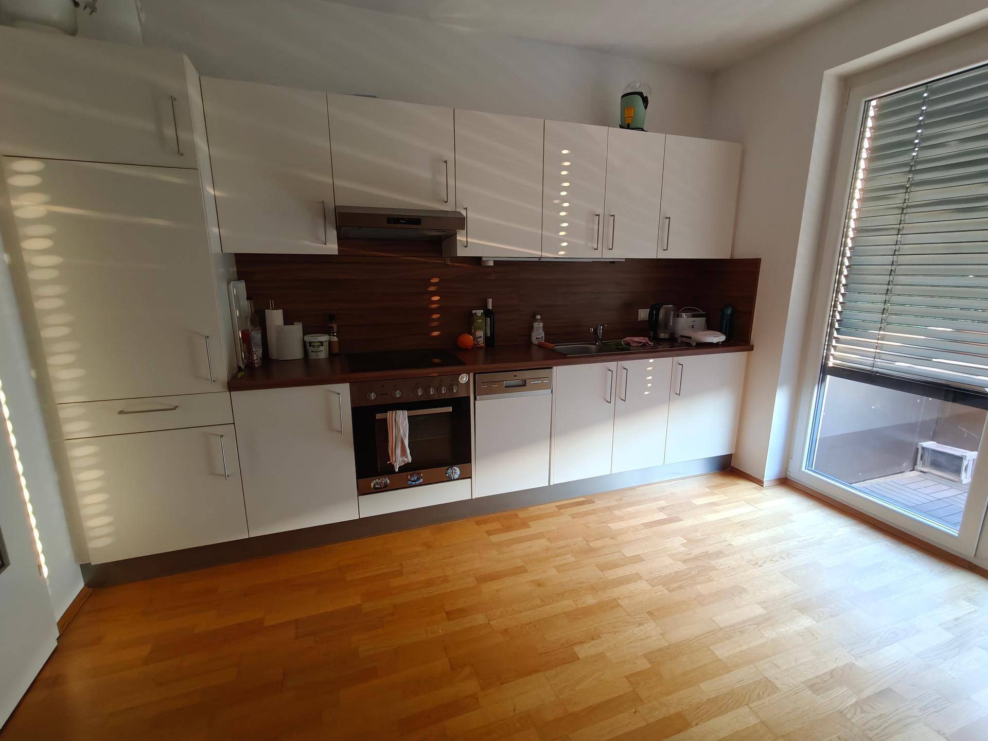Moderne Küche mit weißen Schränken, Holzarbeitsplatte und Zugang zu einem Außenbereich.