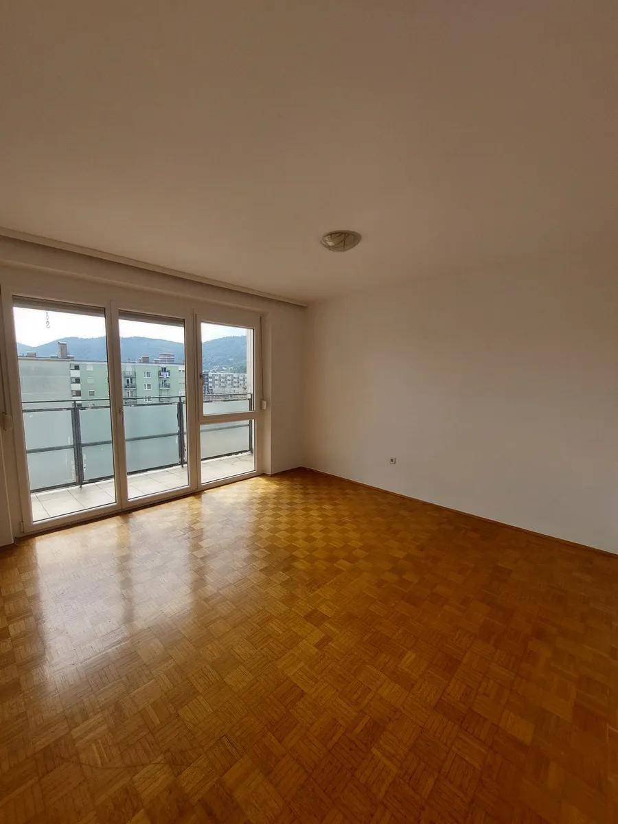 Lichtdurchfluteter Raum mit Parkettboden und breiten Balkontüren, die eine angenehme Atmosphäre schaffen.