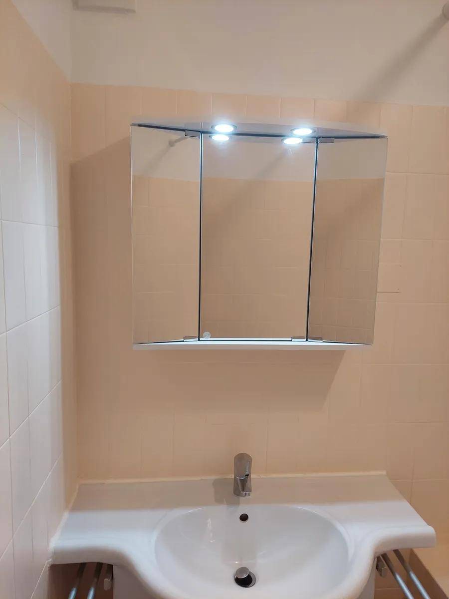 Badezimmer mit Einzelwaschbecken und einem Spiegelschrank darüber, umgeben von beigefarbenen Fliesen.