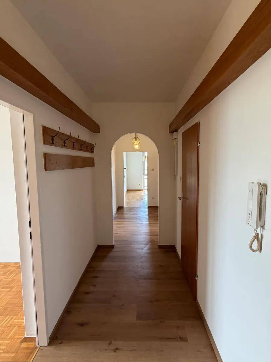 Heller Flur mit Holzboden, weißen Wänden und dekorativen Holzbalken, der zu weiteren Räumen führt.