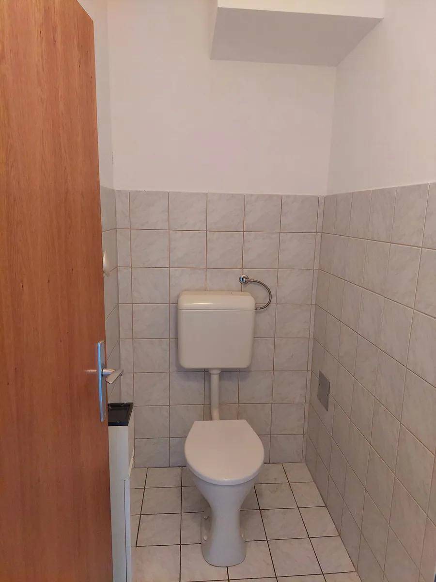 Separate Toilette mit weiß gefliesten Wänden und einem Standard-WC.