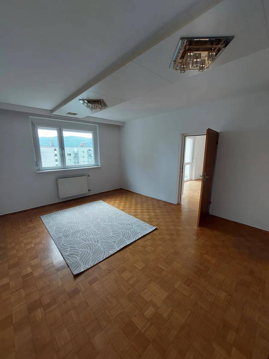 Geräumiger Raum mit Parkettboden, einem Fenster und dekorativen Deckenleuchten.