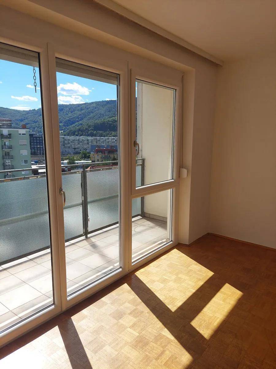 Heller Raum mit Parkettboden und großen Balkontüren, die viel Sonnenlicht hereinlassen und Bergblick bieten.