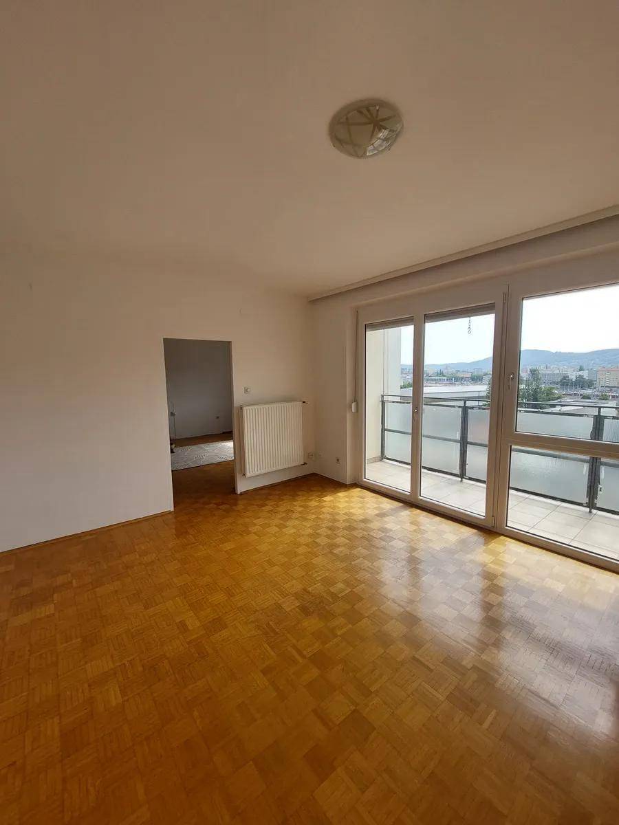 Heller Raum mit Parkettboden und großzügigen Balkontüren, die viel Licht hereinlassen.