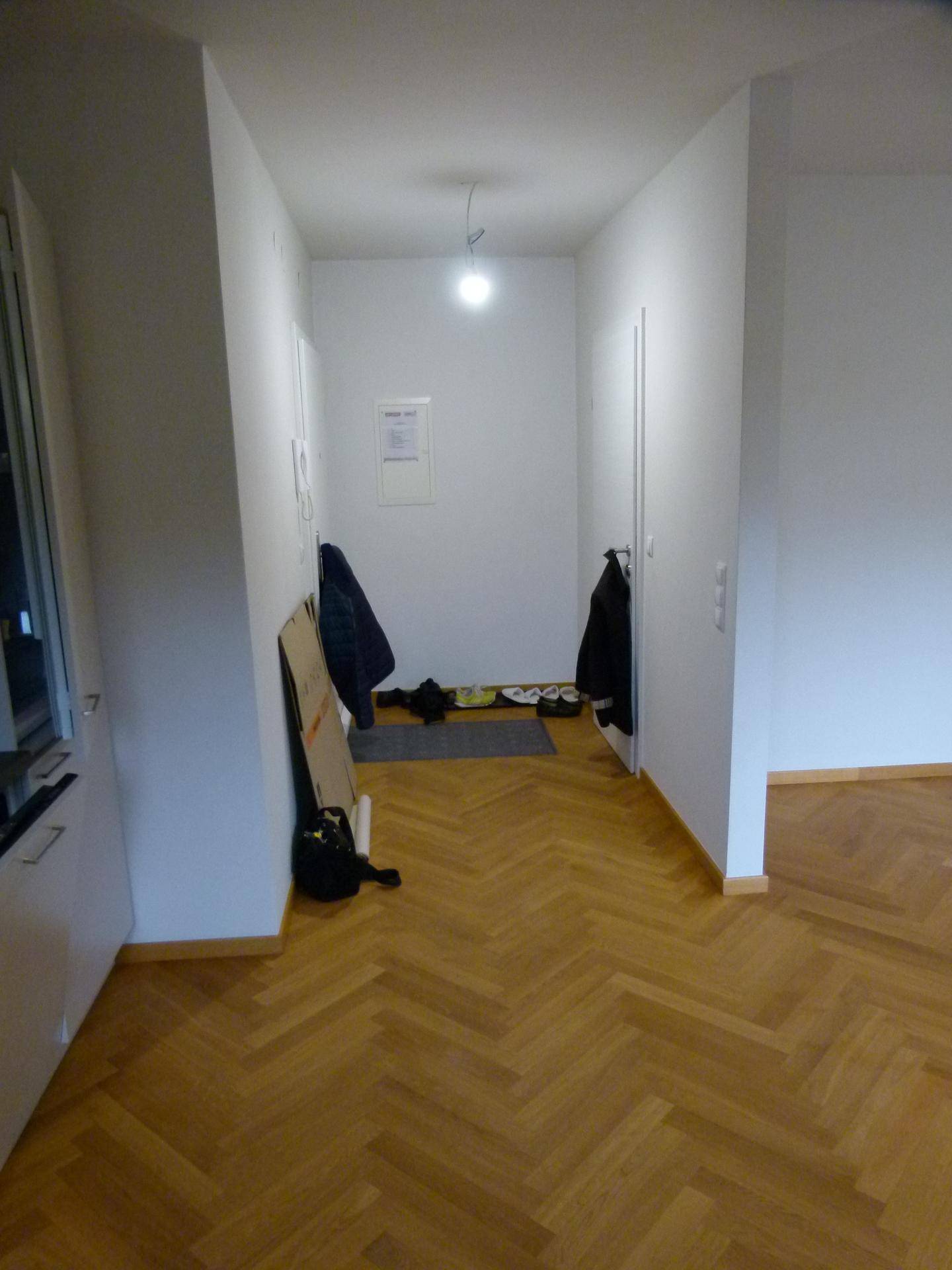 Heller Flur mit Fischgrätparkett und Garderobenbereich, der zu weiteren Räumen führt.