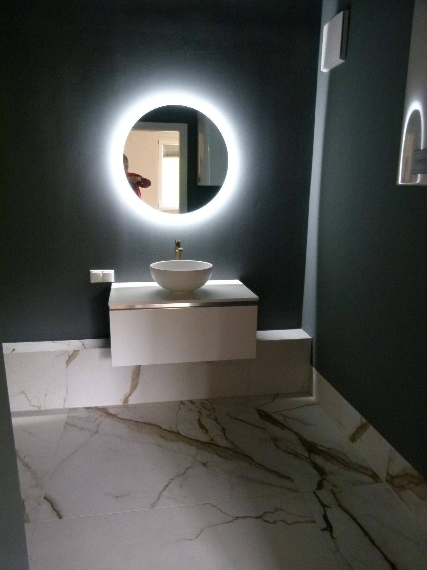 Modernes Badezimmer mit beleuchtetem Spiegel, Aufsatzwaschbecken und Marmorfliesen.