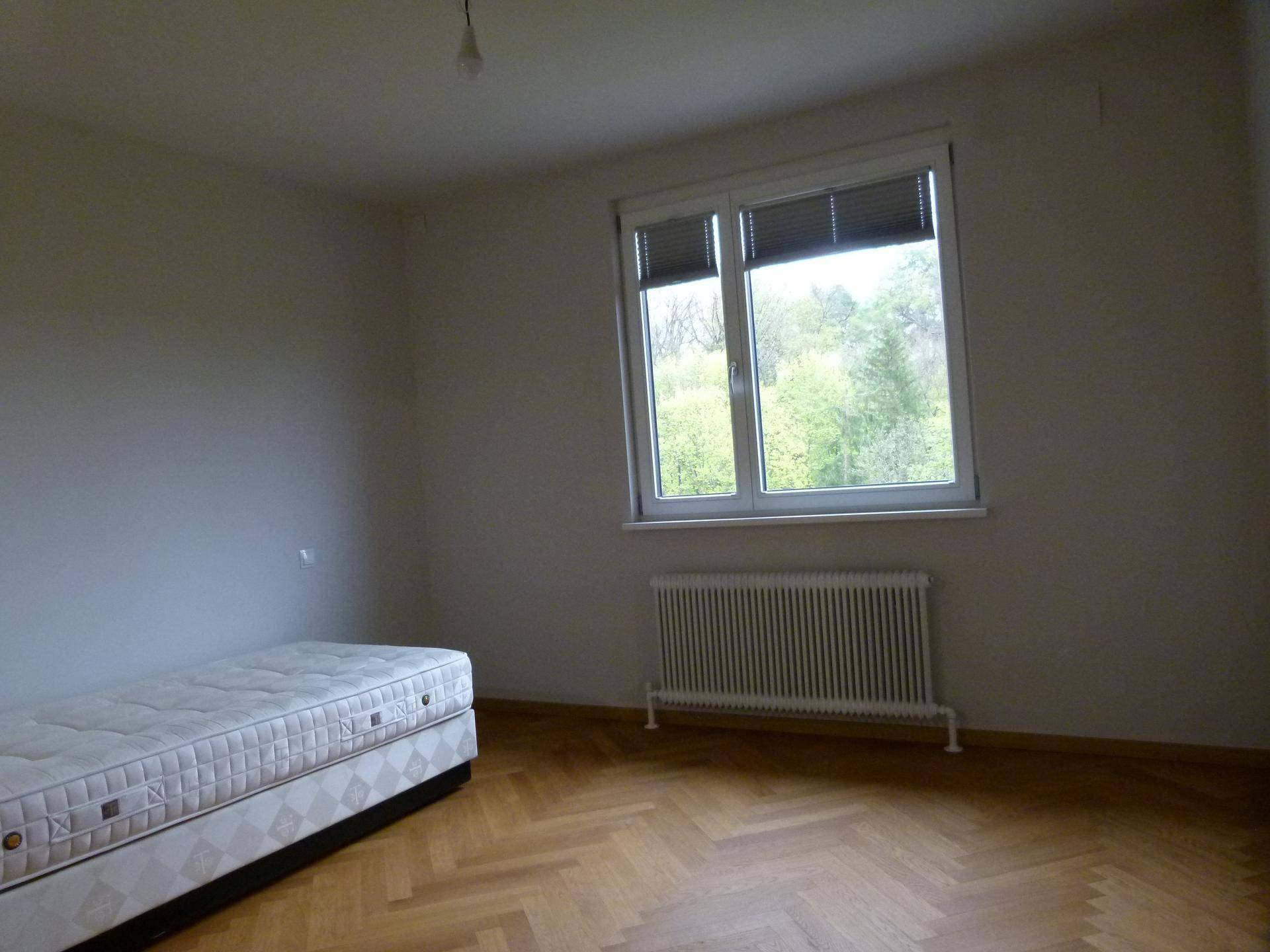 Helles Schlafzimmer mit Parkettboden, Einzelbett und Blick ins Grüne durch das Fenster.