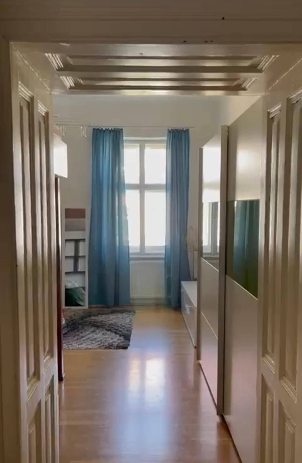 Heller Raum mit Holzfußboden, blauen Vorhängen und einer dekorativen Decke.