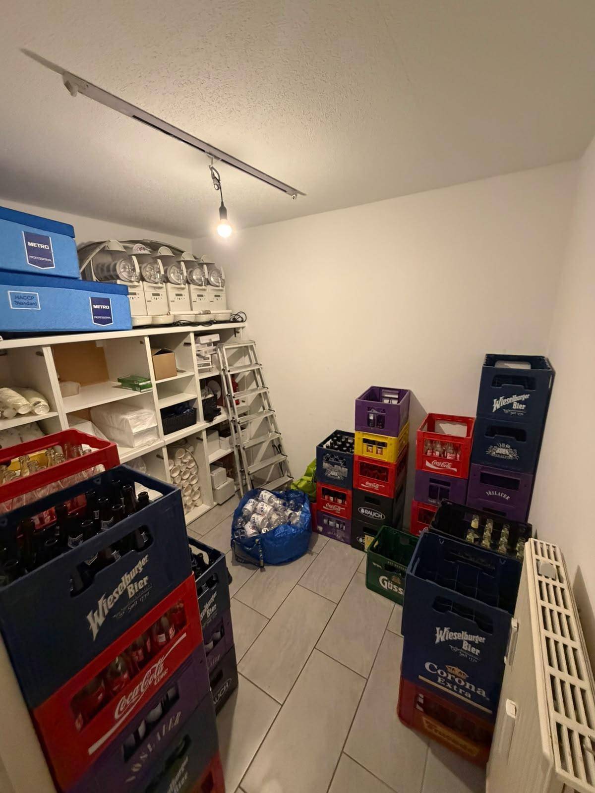 Ein gut gefüllter Lagerraum mit Regalen und zahlreichen Getränkekisten auf dem Fliesenboden.