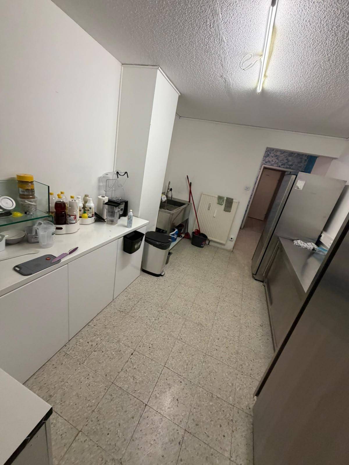 Eine funktionale Gewerbeküche mit weißen Schränken, Edelstahlgeräten und einem gefliesten Boden.