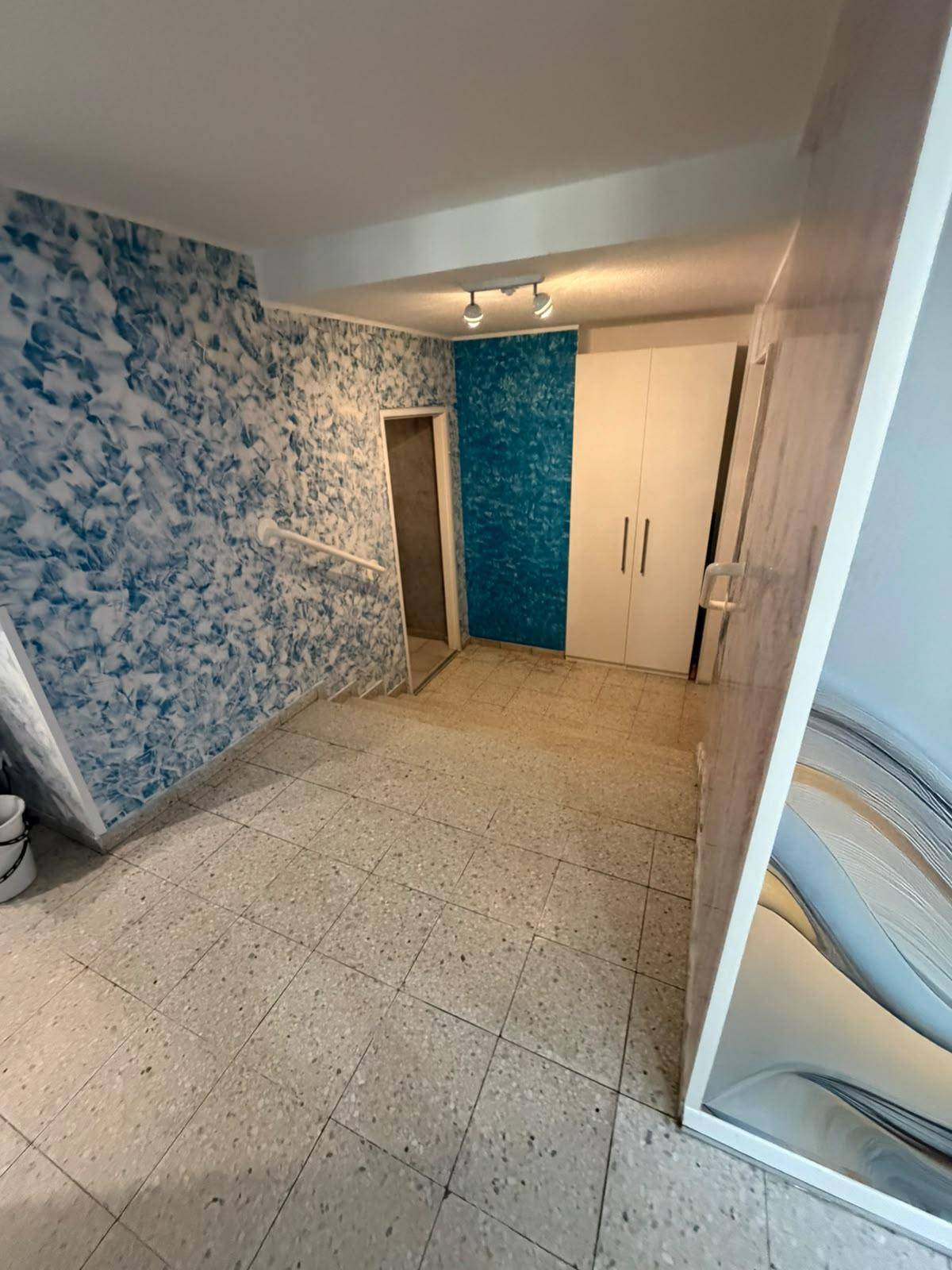 Ein Raum mit blauen, strukturierten Wänden, einem weißen Kleiderschrank und einem hellen Fliesenboden.