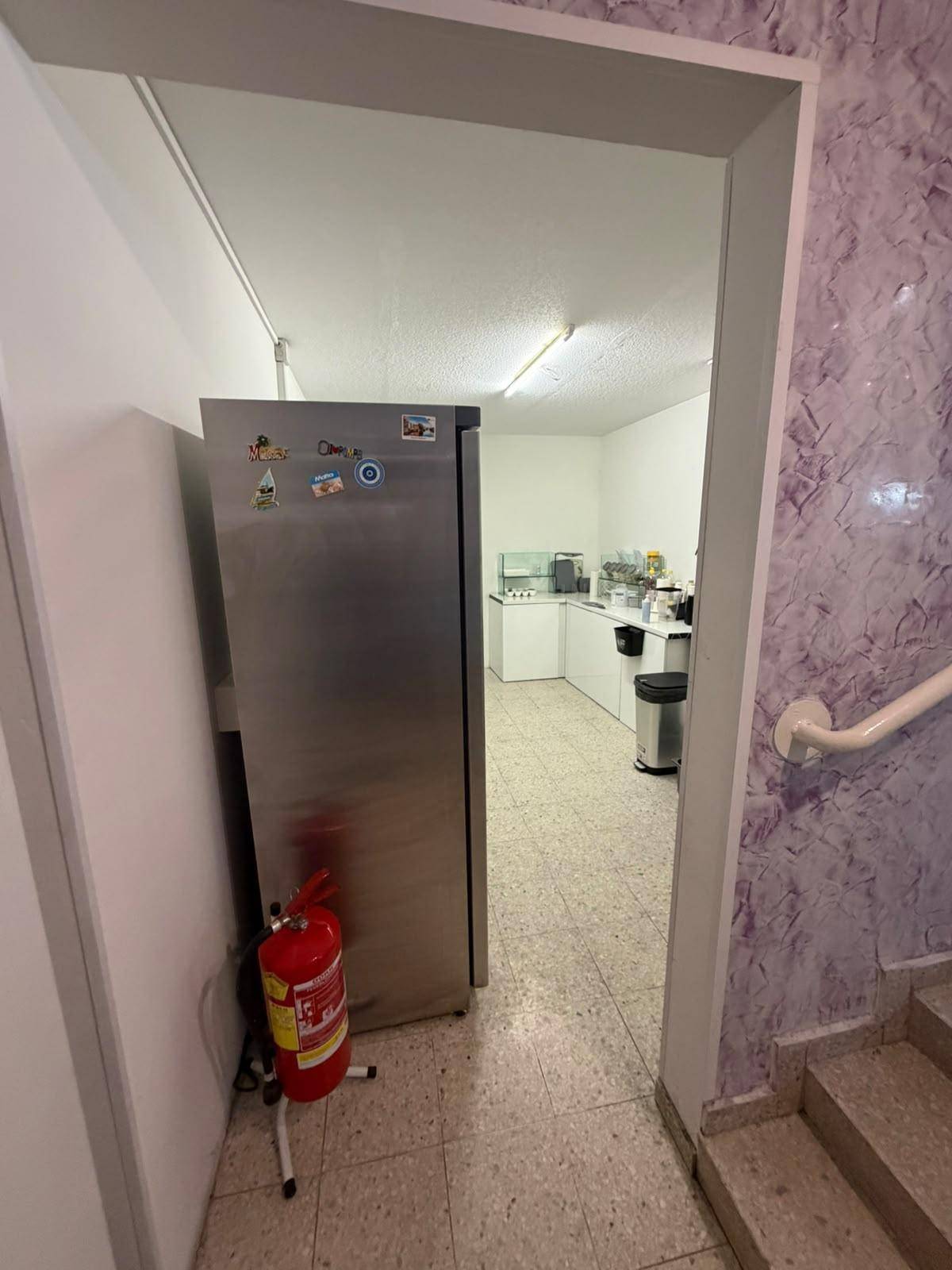 Eingangsbereich zum Küchenbereich mit einem großen Edelstahlkühlschrank und einem Feuerlöscher.