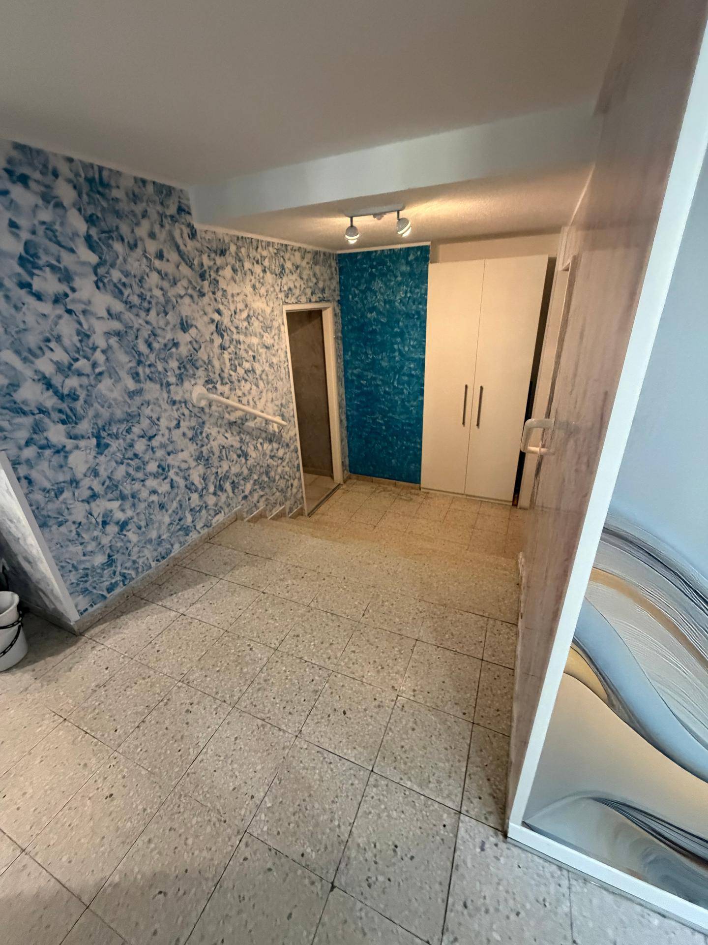 Innenraum mit Fliesenboden und auffälligen blauen Wänden, ausgestattet mit einem weißen Schrank.