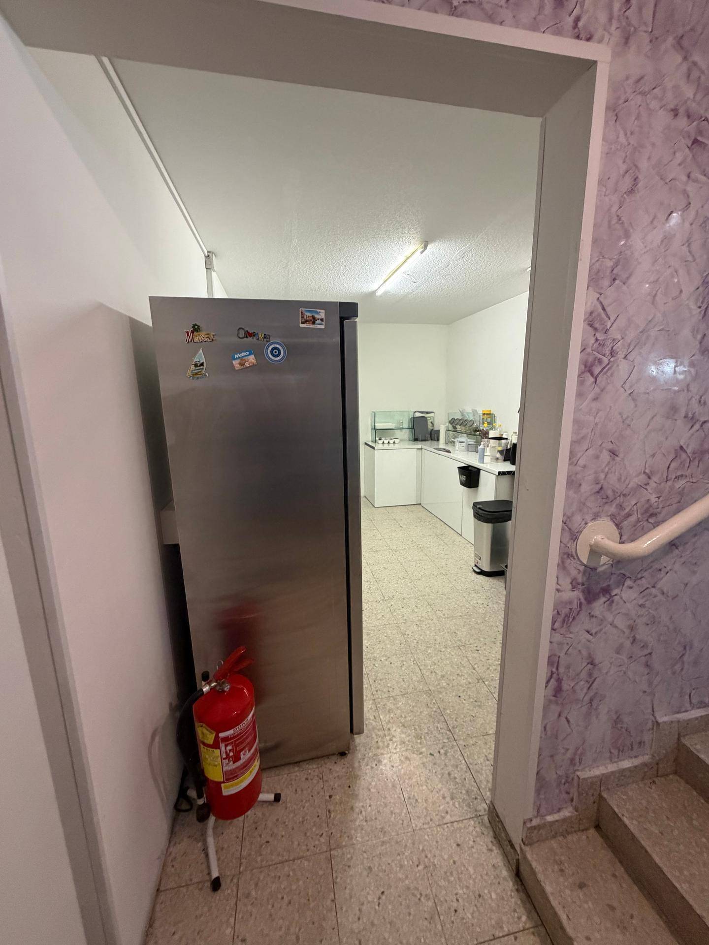 Blick in eine funktionale Küche mit großem Edelstahlkühlschrank und einem Feuerlöscher im Vordergrund.