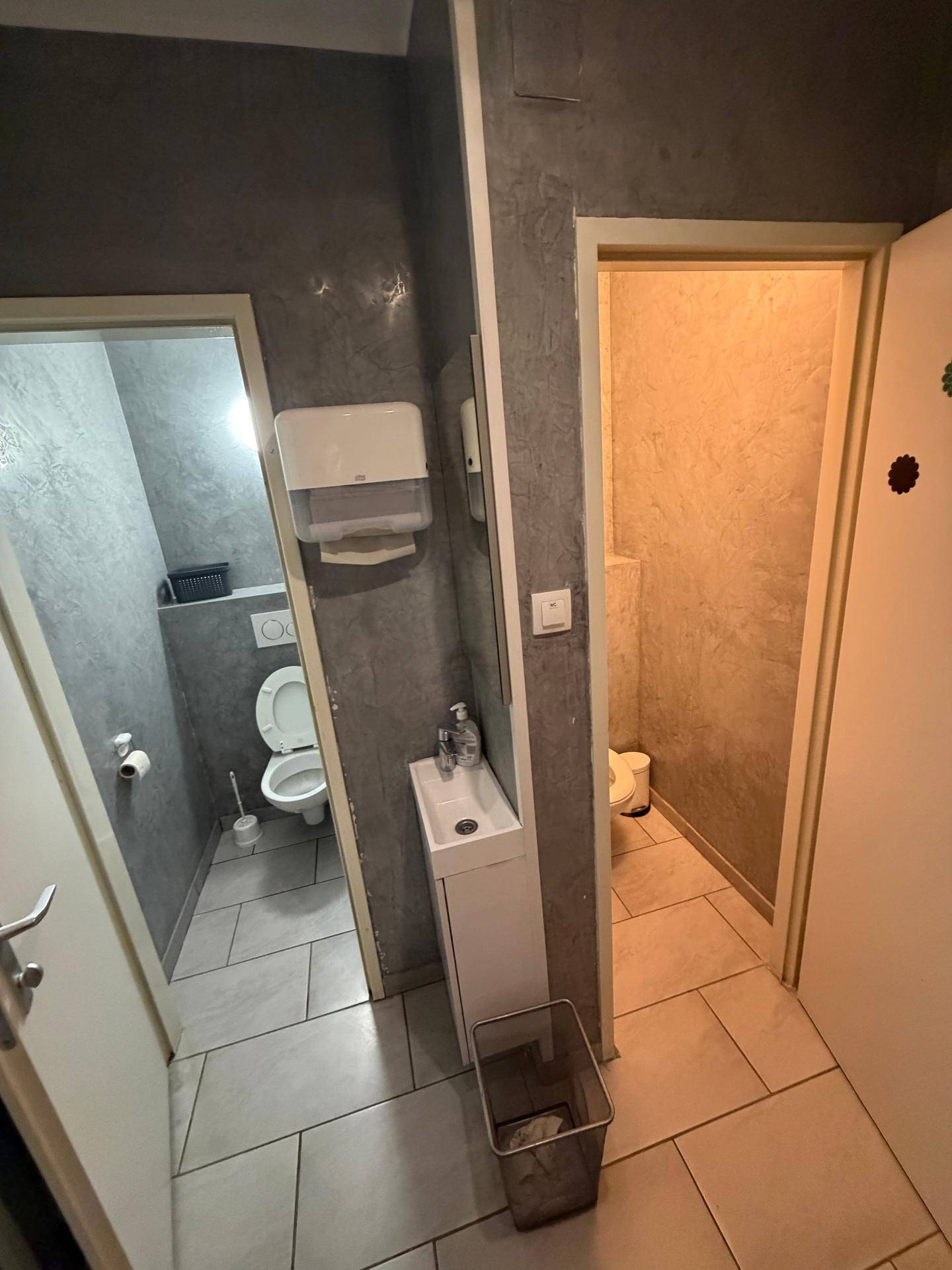Zwei separate Toilettenräume mit einem gemeinsamen Waschbeckenbereich und modernen Fliesen.