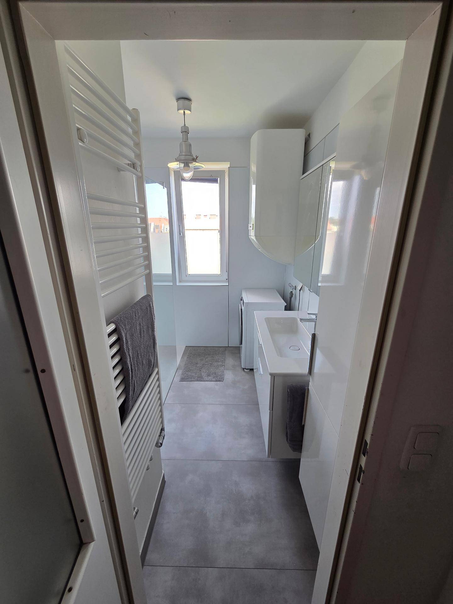 Modernes, schmales Badezimmer mit Fenster, Waschbecken und beheiztem Handtuchhalter.