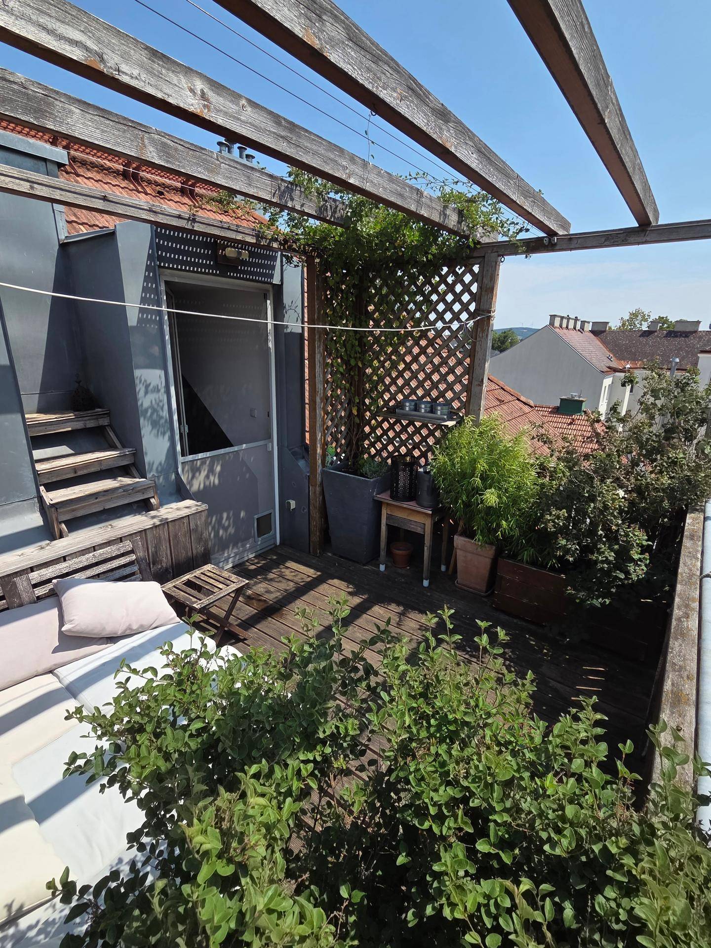Sonniger Terrassenbereich mit Holzpergola, üppigen Pflanzen und bequemen Outdoor-Möbeln.
