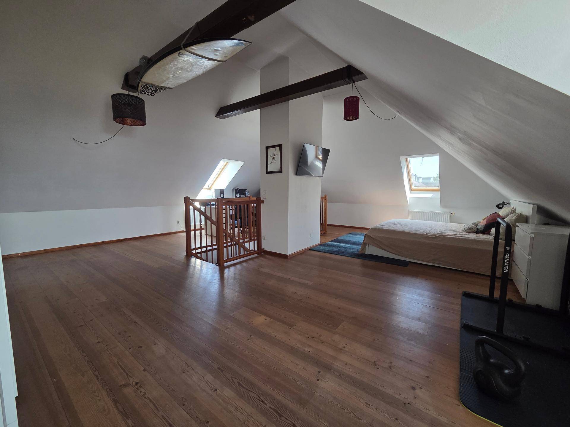 Heller Dachbodenraum mit Holzboden, Dachschrägen und einem Schlafbereich unter den Dachfenstern.
