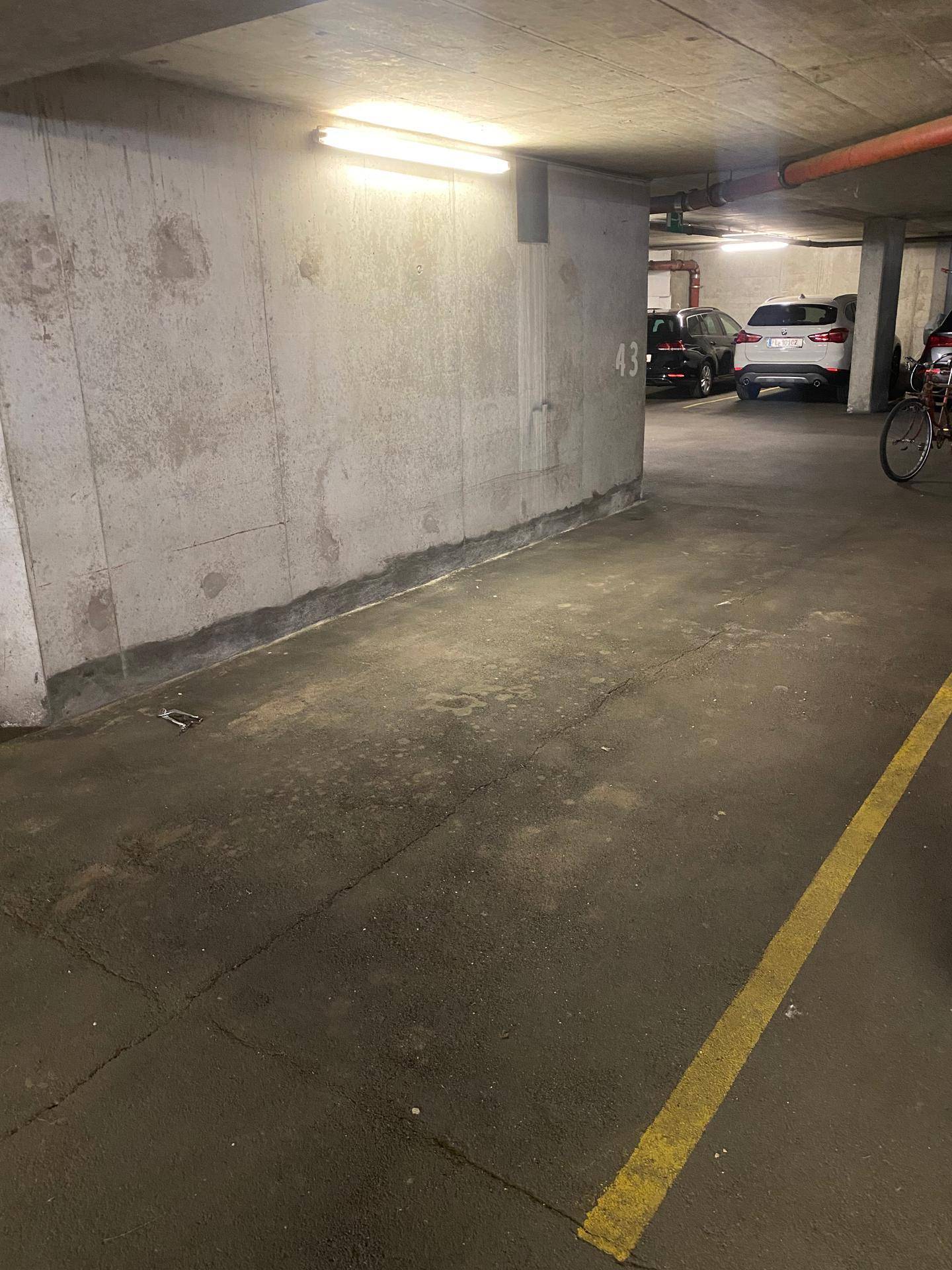 Blick in die Tiefgarage mit geparkten Autos und Betonwänden.