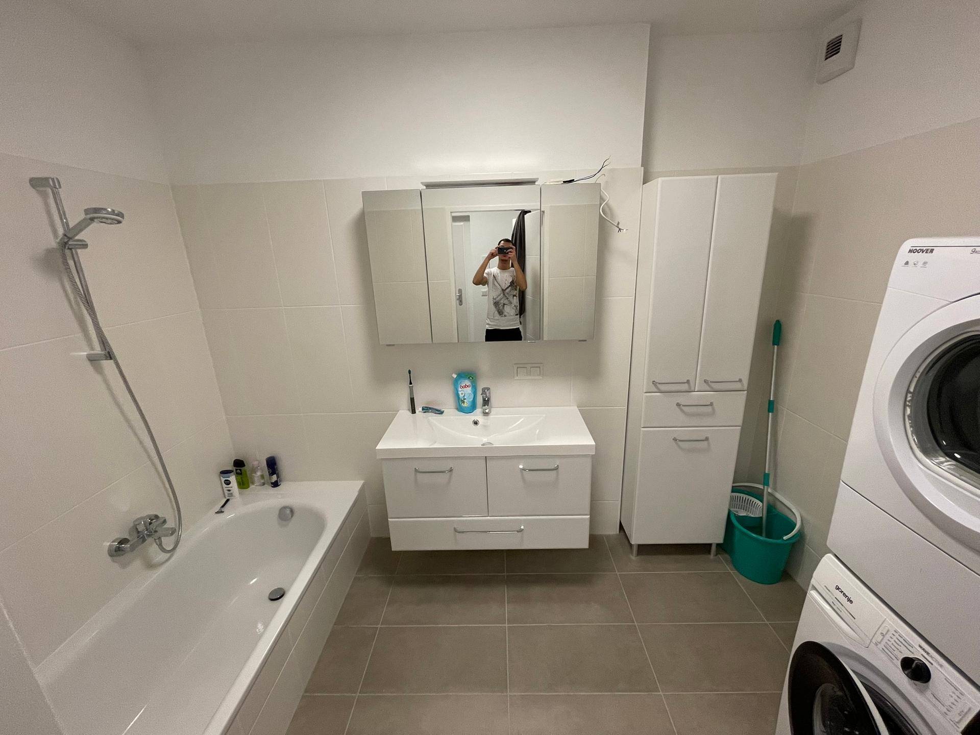 Geräumiges Badezimmer mit Badewanne, Waschtisch, Spiegelschrank und Waschmaschine.