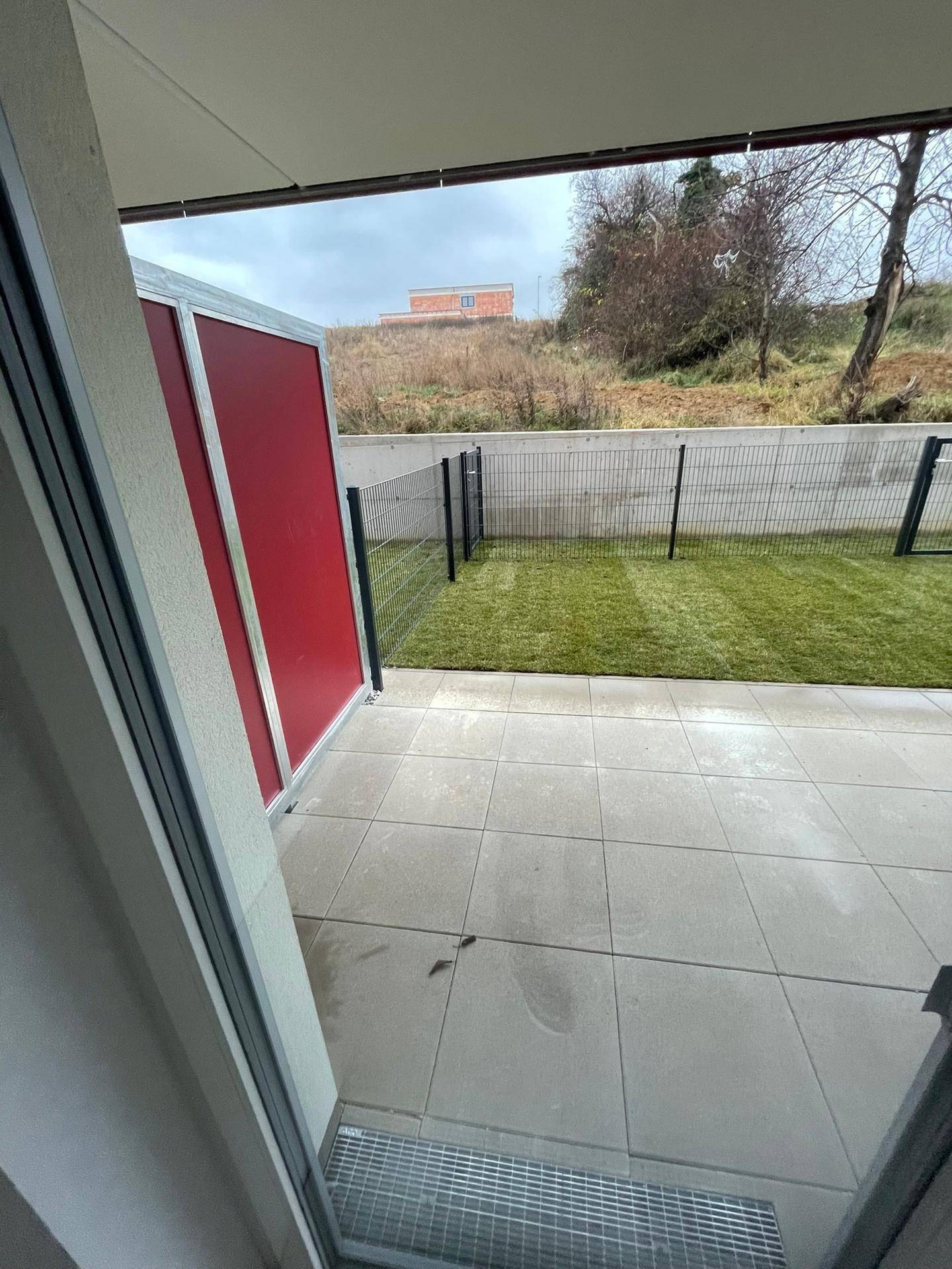 Geflieste Terrasse mit kleinem Rasenbereich und Blick auf die grüne Umgebung.