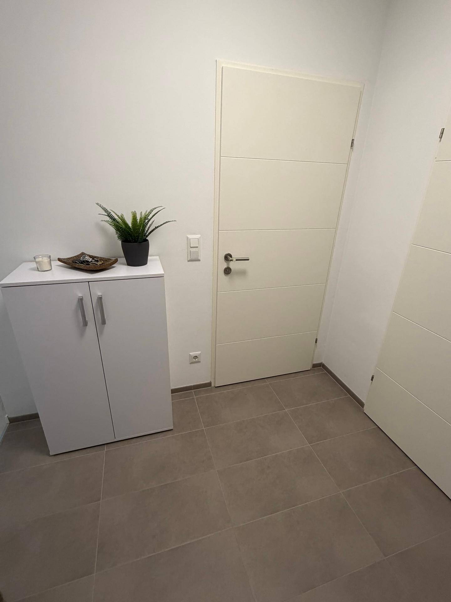 Schlichter Flur mit hellem Fliesenboden und einem kleinen weißen Schrank.