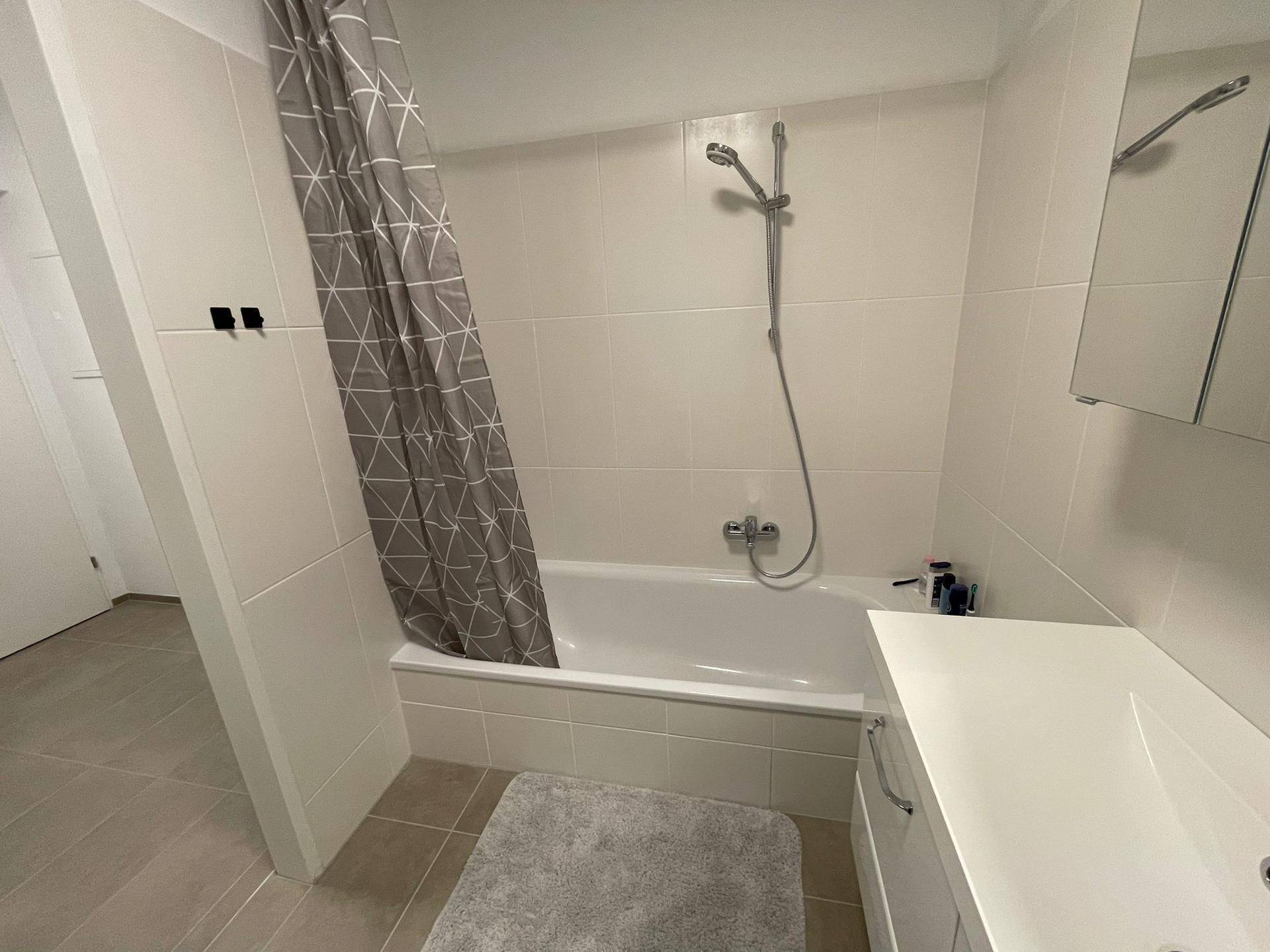 Helles Badezimmer mit Badewanne, Duschvorhang und modernem Waschtisch.