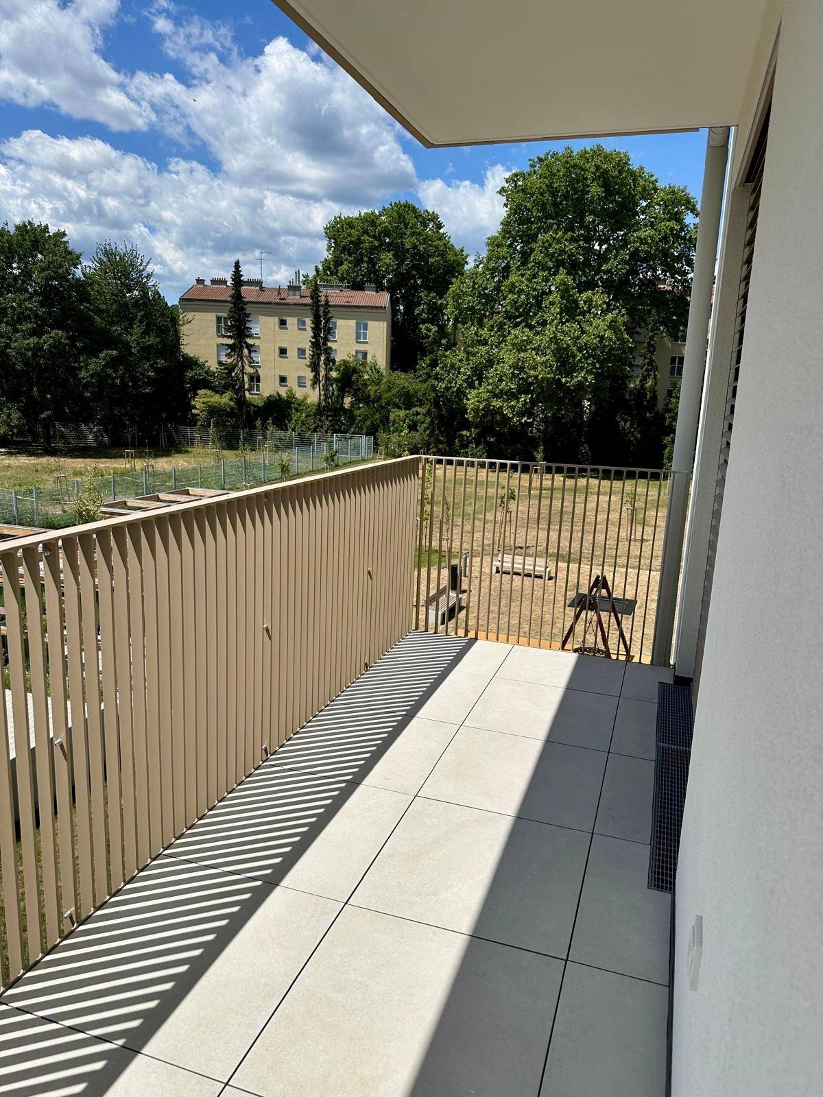 Langer Balkon mit Fliesenboden und sonnigem Ausblick auf eine Grünfläche.
