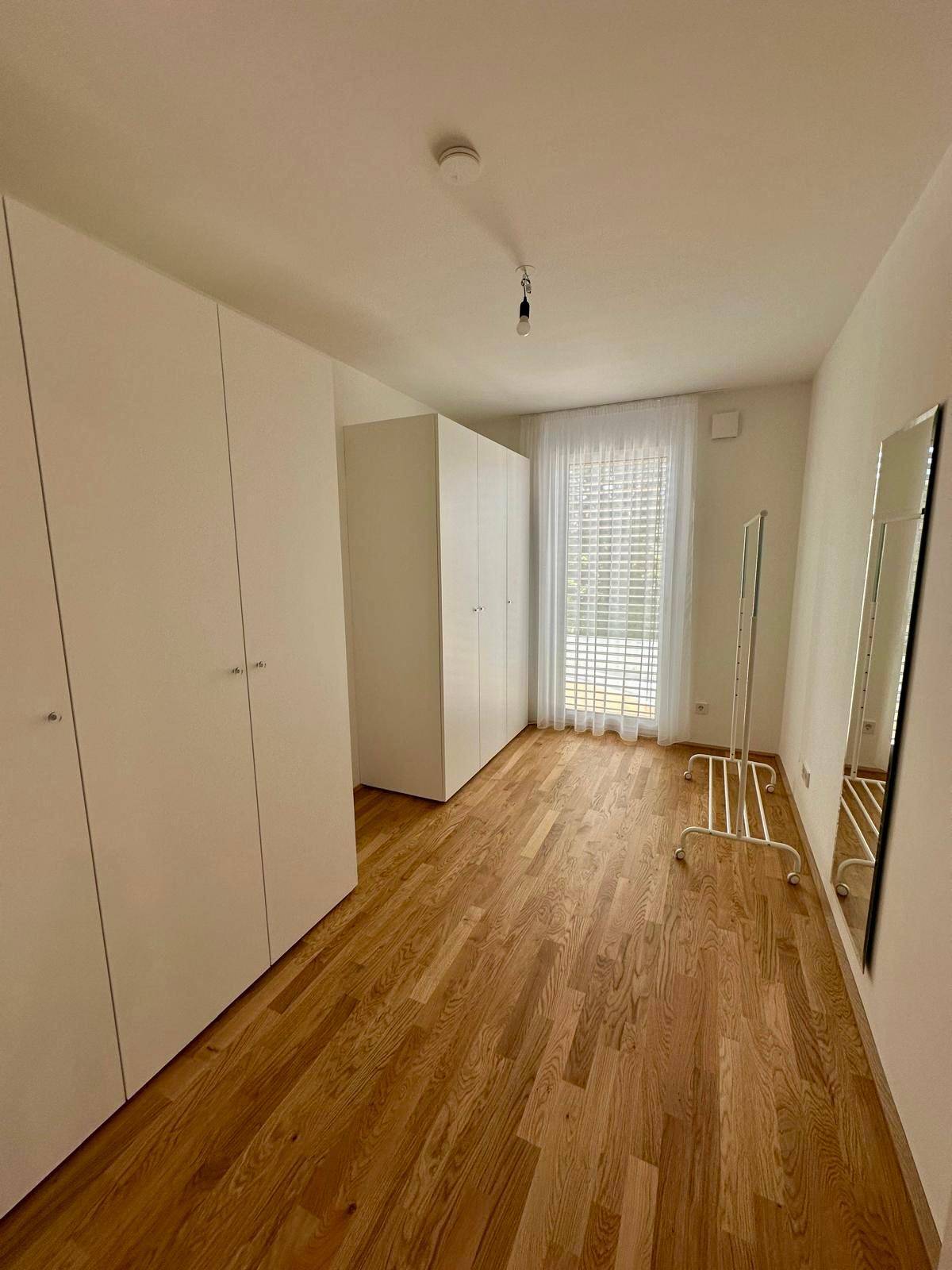 Geräumiges Schlafzimmer mit Holzboden, weißen Schränken und großen Fenstern.