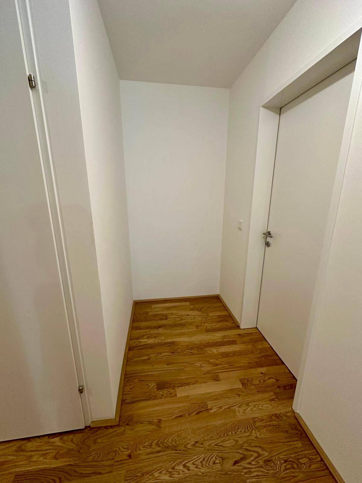 Heller Flur mit elegantem Holzparkettboden und weißen Wänden, der verschiedene Räume verbindet.
