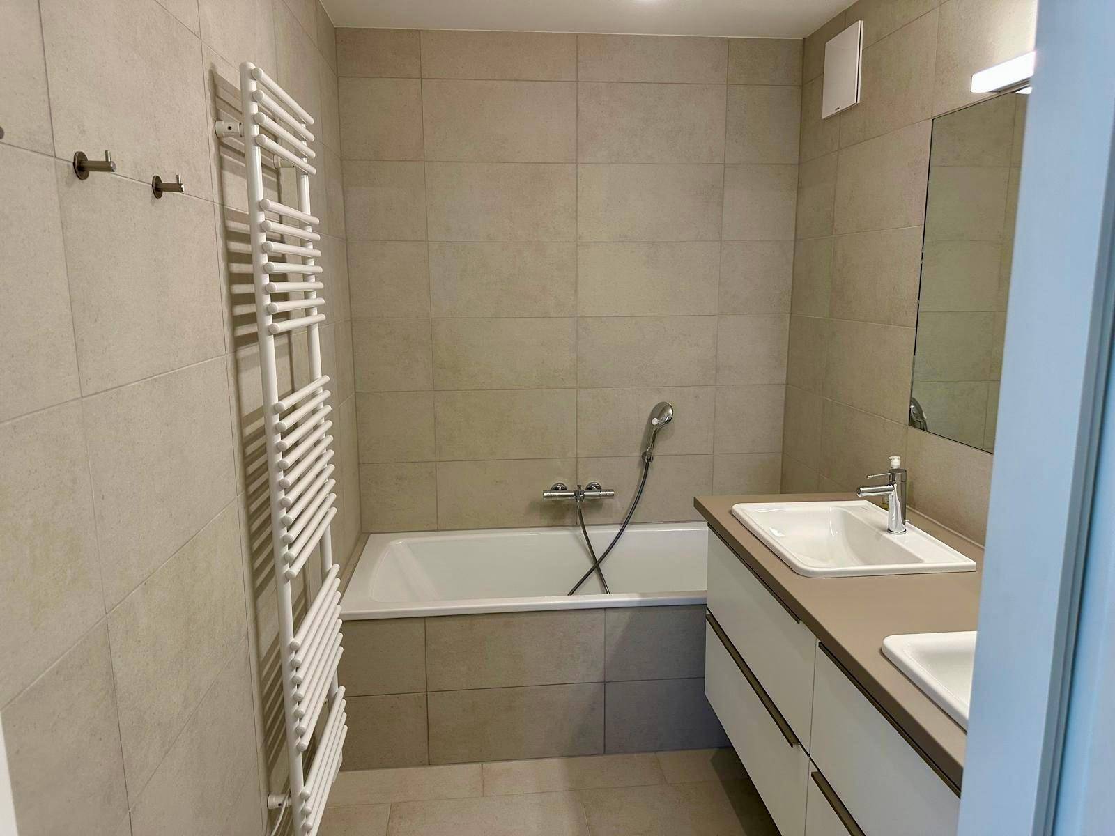 Modernes Badezimmer mit Badewanne, Doppelwaschbecken und hellen Wandfliesen.