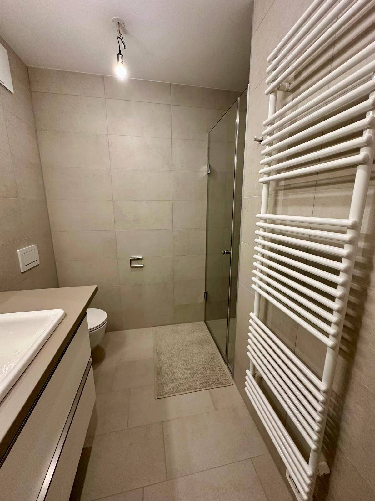 Modernes Badezimmer mit begehbarer Dusche, Glasabtrennung und einem praktischen beheizten Handtuchhalter.