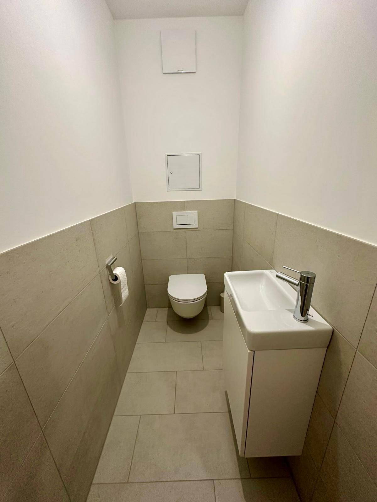 Modernes Gäste-WC mit wandhängender Toilette und kleinem Waschbecken, ausgestattet mit hellen Fliesen.