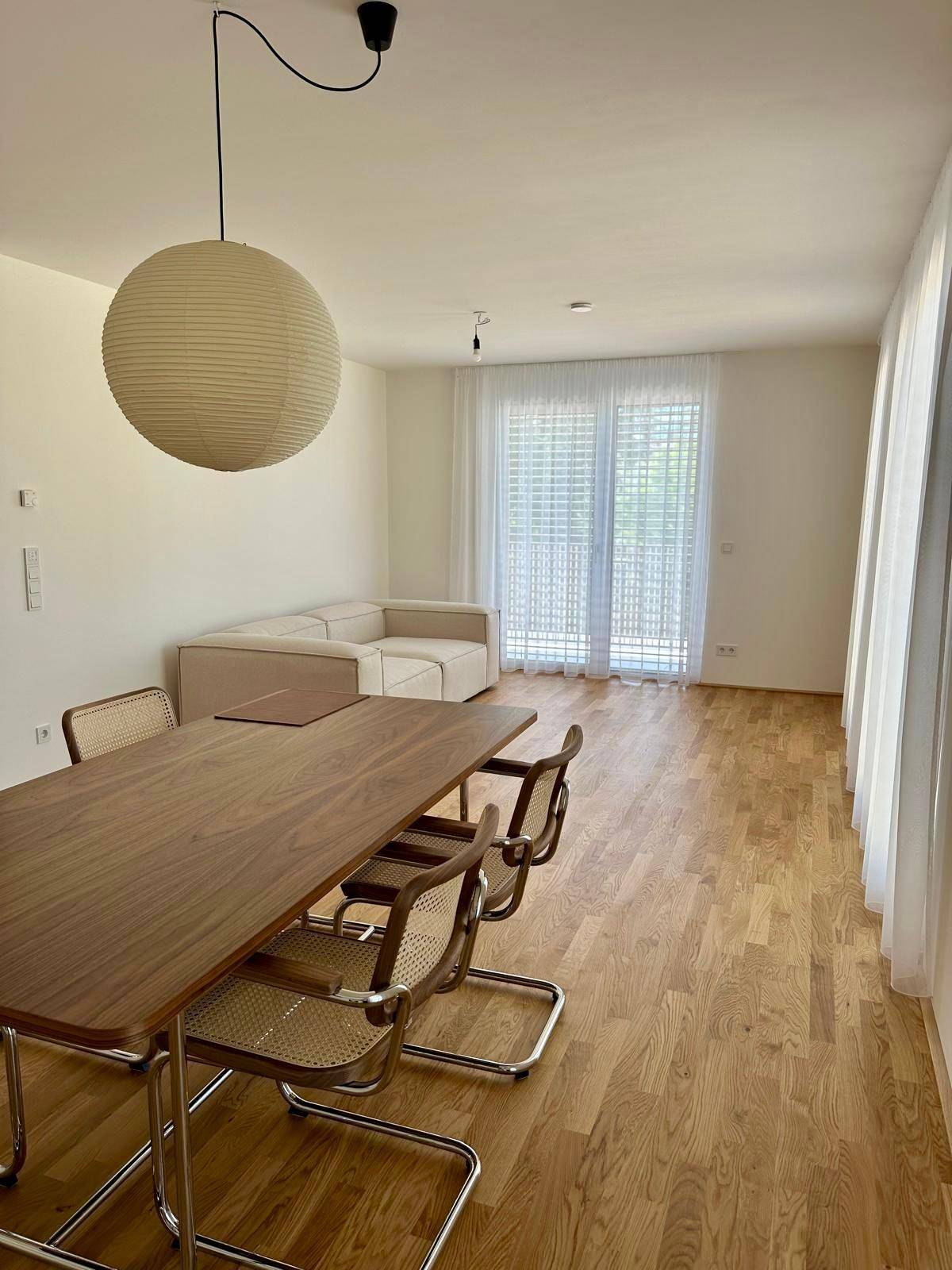 Heller Wohnbereich mit Holzboden, beiger Couch und Zugang zum Balkon.