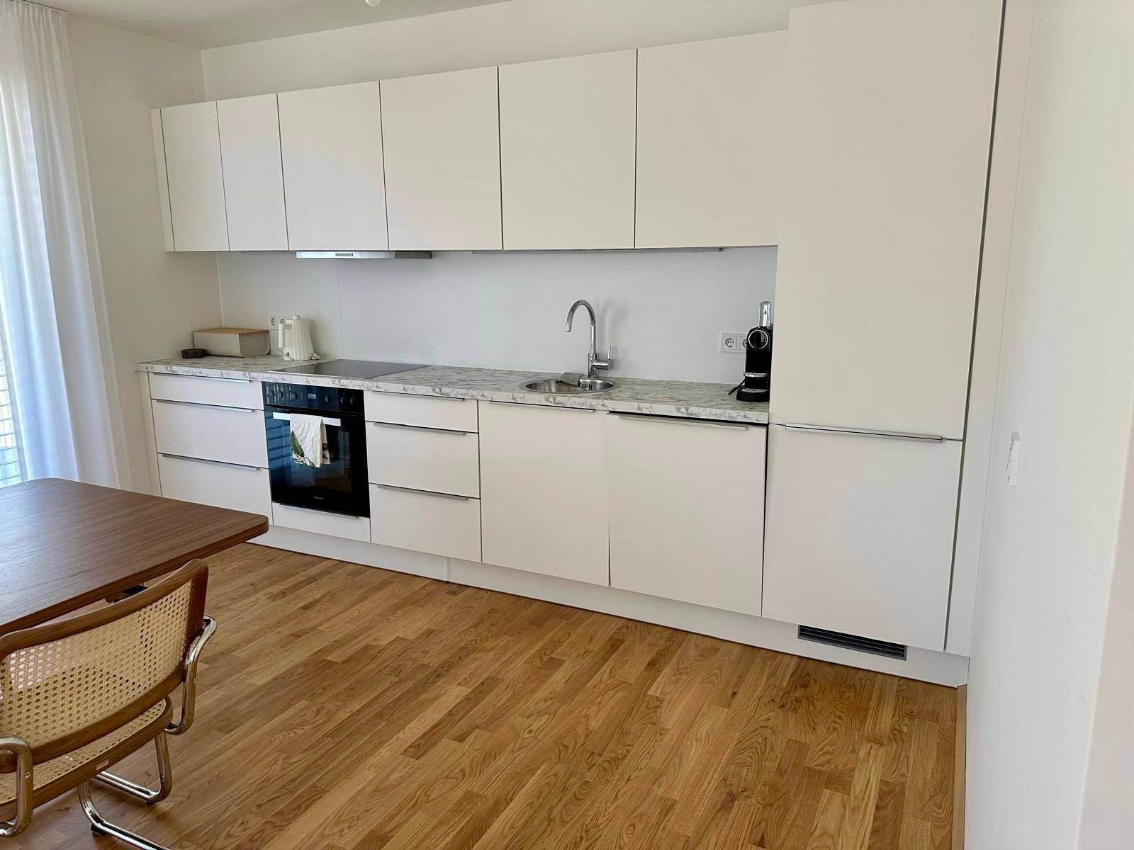 Moderne Einbauküche mit weißen Fronten, Granitarbeitsplatte und Holzboden.