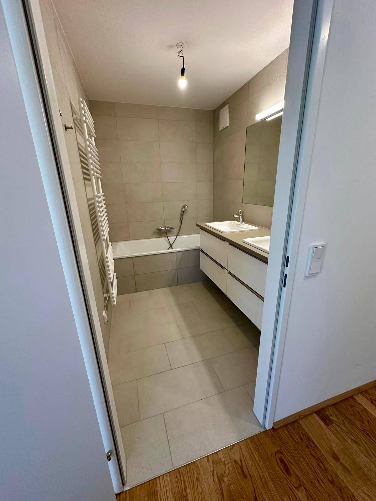 Modernes Badezimmer mit Badewanne, Doppelwaschbecken und hellen Fliesen.