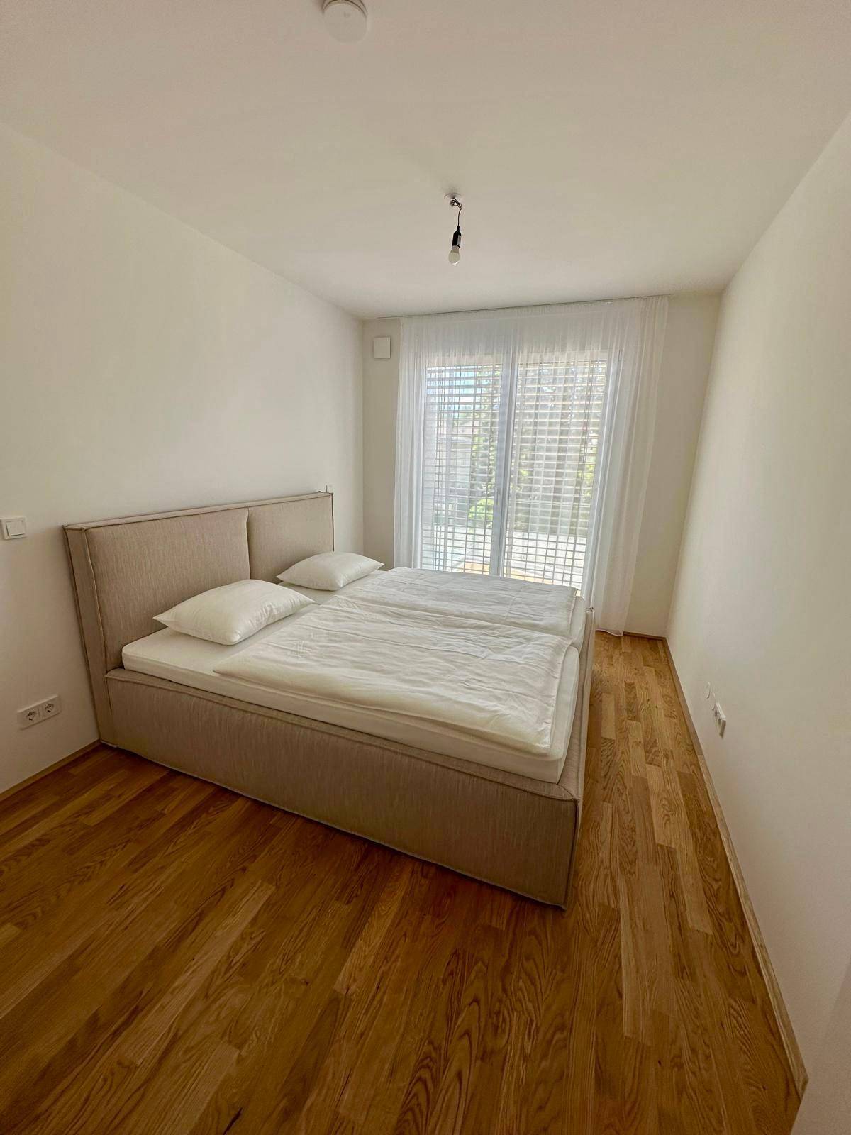 Helles Schlafzimmer mit Doppelbett, Holzboden und großen Fenstern.