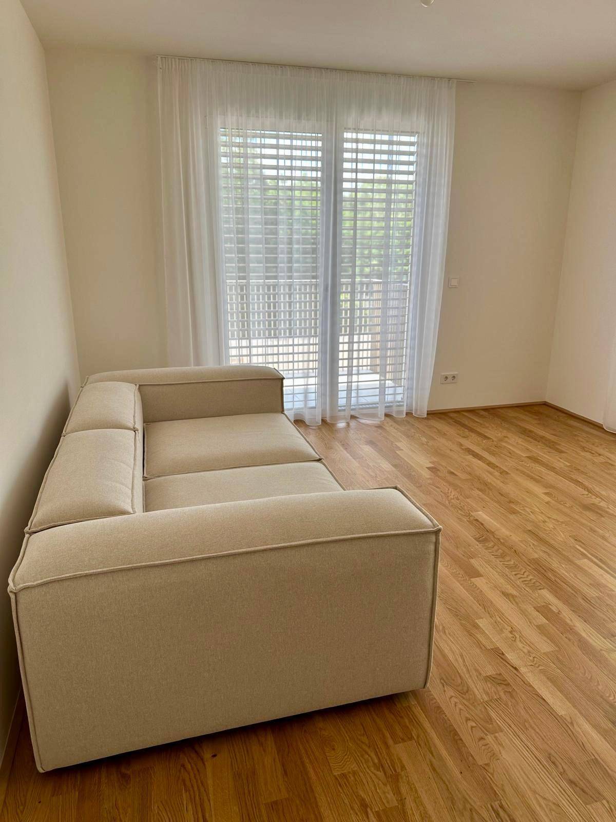 Gemütlicher Wohnbereich mit beiger Eckcouch und Zugang zum Balkon.