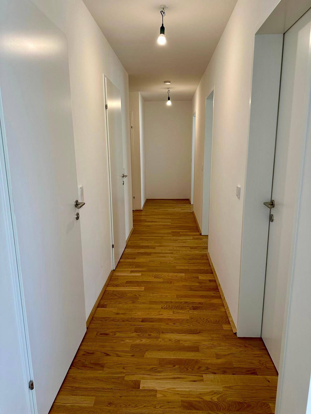 Langer, heller Flur mit Holzboden und mehreren Türen.